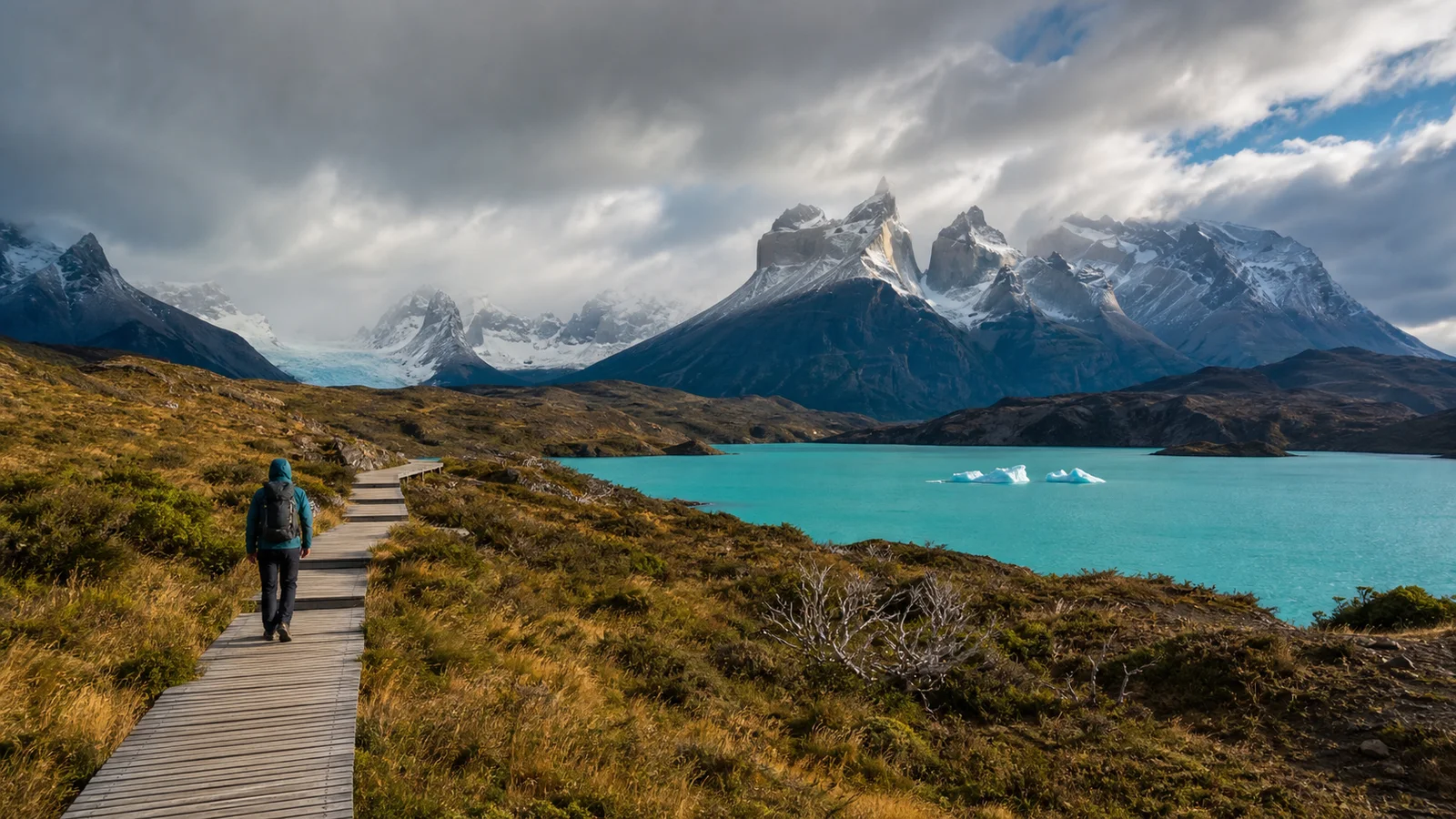 Editorial image of a Patagonia boardwalk trail, turquoise water, and snow-dusted mountains.